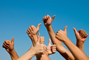 Group of people giving thumbs up over blue sky